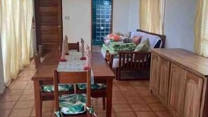 A dining area with a wooden table and chairs, a cabinet, and a window with curtains. - Paradise Beach Belize Suite B (downstairs) (Hopkins)
