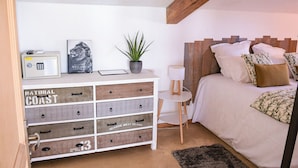 Ein Schlafzimmer mit einem Bett, einem Nachttisch, einer kleinen weißen Lampe, einem Radio, einem gerahmten Bild und einer Pflanze.