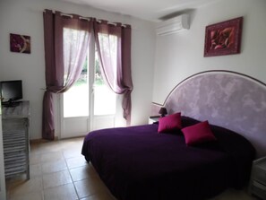 A bedroom with a bed, curtains, a television, and artwork on the walls. - Résidence Rocca Rossa Mini Villa 4/5 Personnes Palombaggia (Porto-Vecchio)