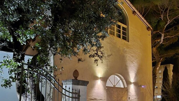 Un edificio con facciata in pietra, un ingresso con cancello e una piccola veranda con piante in vaso.