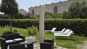 Un'area esterna con posti a sedere in vimini, un ombrellone bianco e vista su un edificio sullo sfondo.