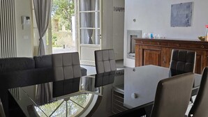 Zona pranzo moderna con tavolo in vetro e sedie nere, camino e vista attraverso un'ampia finestra ad arco.