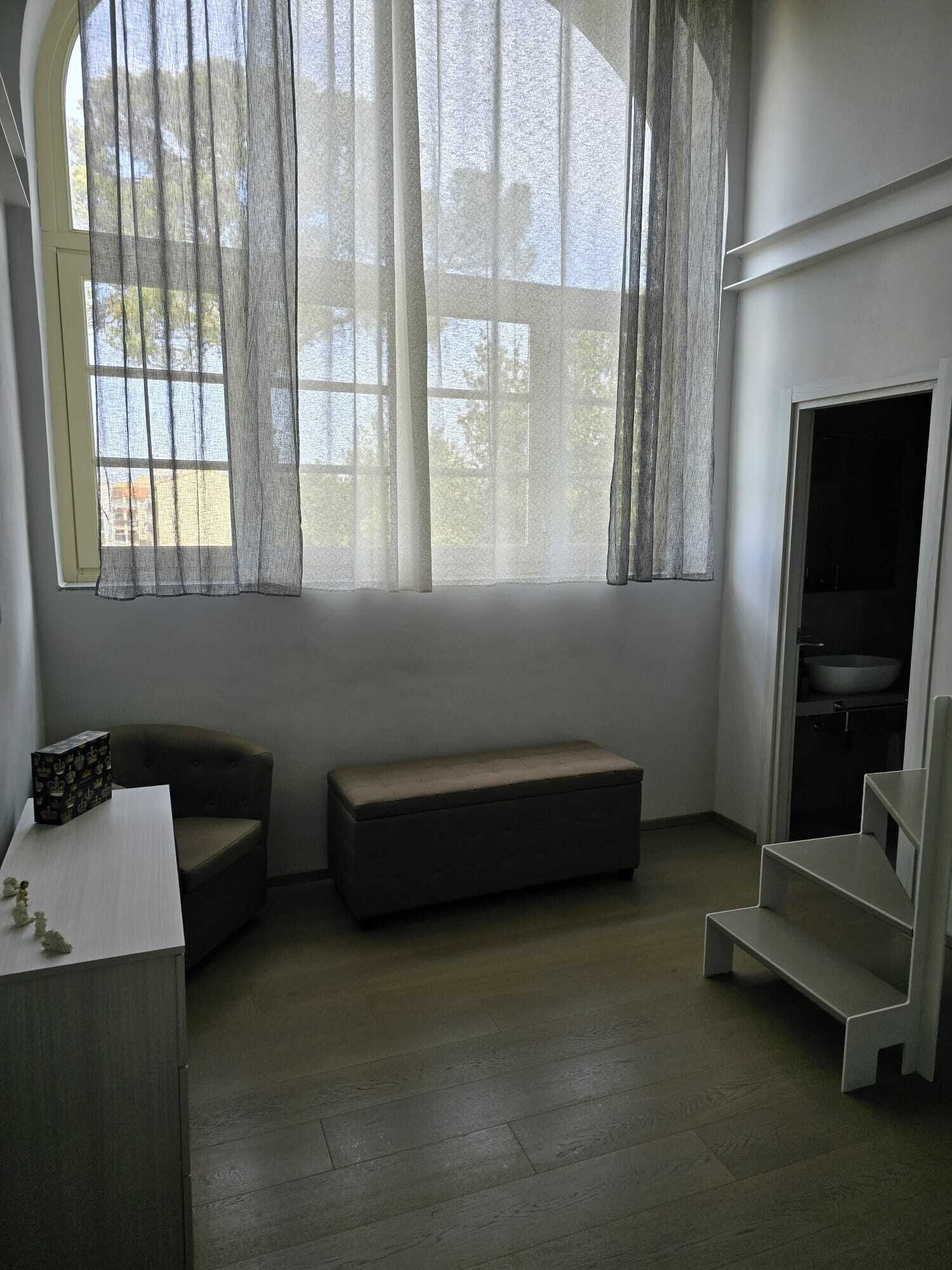 A room with a large window, a bench, a small table, and a built-in sink.