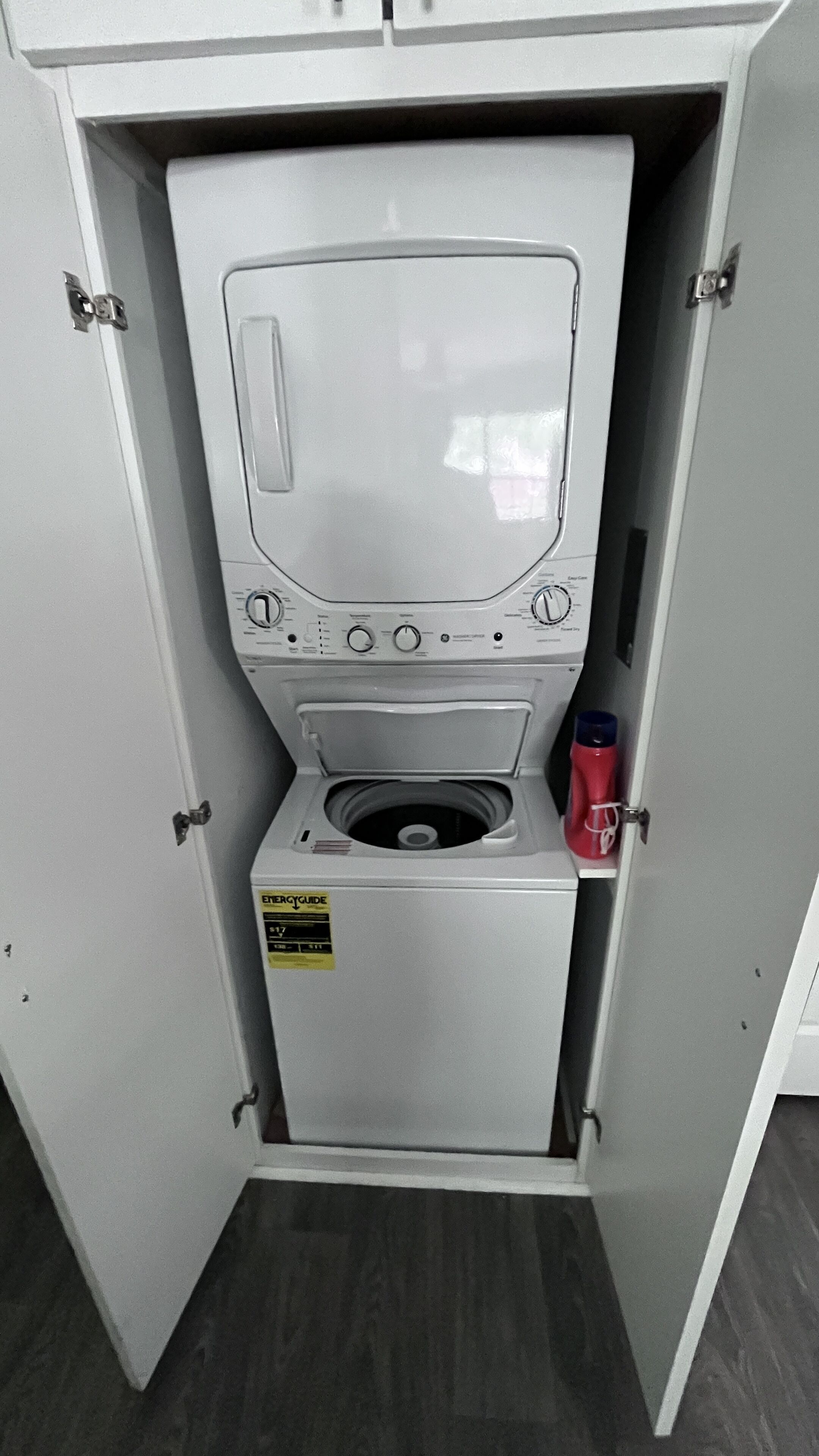 A compact, white laundry room with a front-loading washing machine and a small cabinet below.