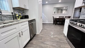 A modern kitchen with white cabinets, a dishwasher, a stove, and a dining area with a table and chairs. - A Home Stay on Business Trip - Near Airport (Atlanta)