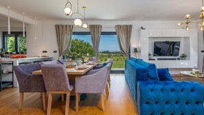 A modern living room with a blue sofa, a dining area with a wooden table and chairs, and a TV mounted on a white cabinet. - Villa Lux Zadarvillas (Zemunik Donji)