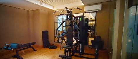 Un gimnasio con equipo de ejercicio, una banca y un espejo grande.