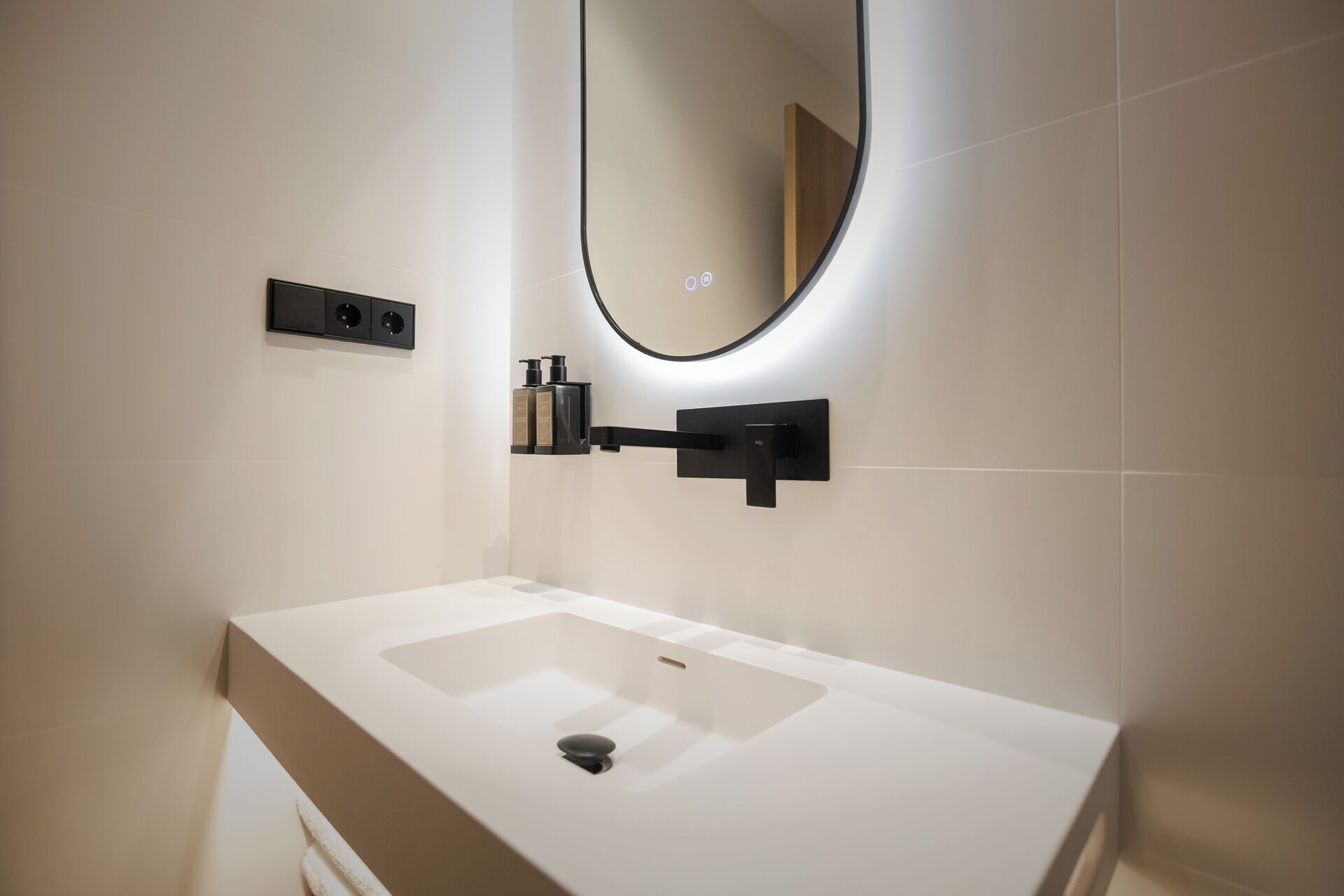 Un baño moderno con un lavabo blanco, un espejo de marco negro y un dispensador de jabón negro en la pared.