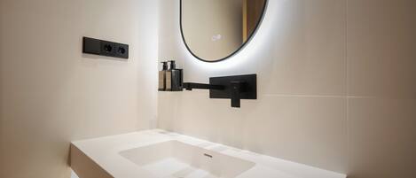 Un baño moderno con un lavabo blanco, un espejo de marco negro y un dispensador de jabón negro en la pared.