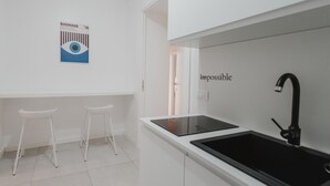 A modern kitchen with white cabinetry, two white stools, a black faucet, and a Bauhaus poster on the wall. - Art Home Collection by Wonderful Italy - Pop Studio (Cefalù)