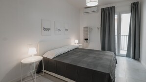 A modern bedroom with a large bed, a bedside table with a lamp, a wardrobe, and a balcony with curtains. - Art Home Collection by Wonderful Italy - Pop Studio (Cefalù)