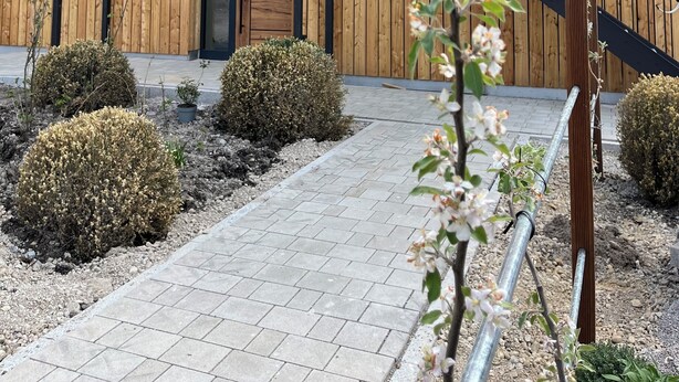 Puinen rakennus, jossa on parveke, portaikko ja päällystetty kävelytie, jonka varrella kasvaa pensaita.