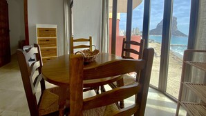 Un comedor con una mesa y sillas, una cesta sobre la mesa, y vistas a la playa y el océano a través de amplios ventanales.