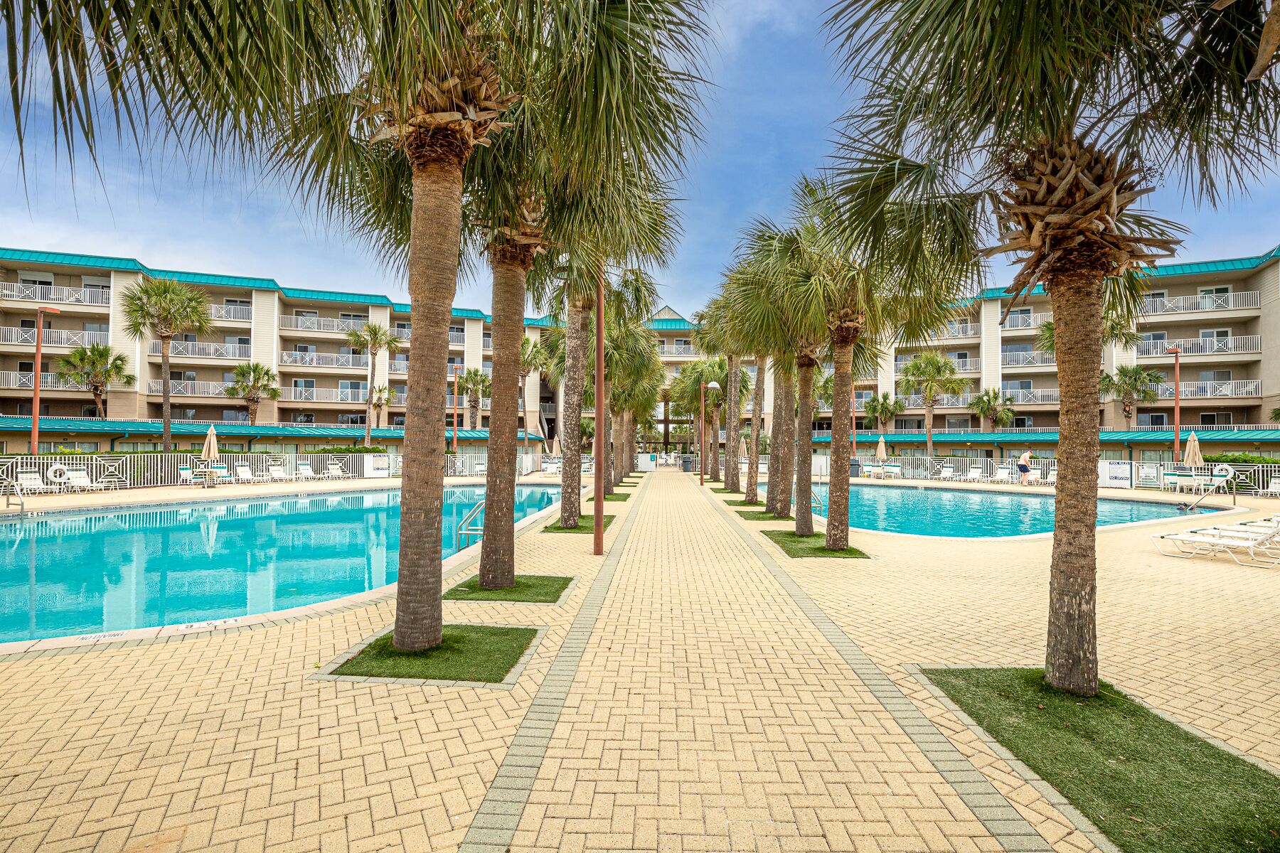 A hotel with a swimming pool, palm trees, and a brick pathway.