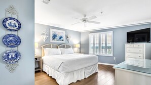 Un dormitorio con cama, mesitas de noche, ventilador de techo, televisor y placas decorativas en la pared.