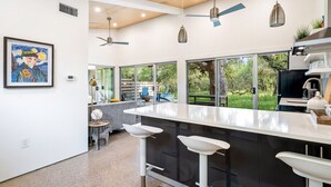 A modern kitchen with a large island, bar stools, and a view of the outdoors. - Chic Barndo • Heated Pool, Firepit, Trails, Stars (Dripping Springs)