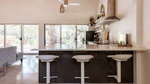 A modern kitchen with a large island, bar stools, and a view of the outdoors. - Chic Barndo • Heated Pool, Firepit, Trails, Stars (Dripping Springs)