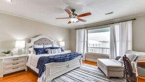 Ein Schlafzimmer mit Bett, Nachttischen, einem Sessel, einem Fenster mit Vorhängen und einem Deckenventilator.