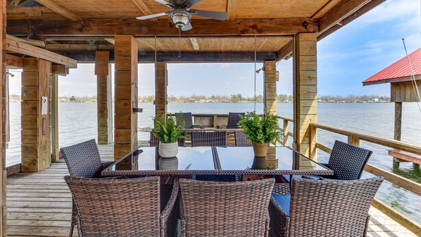 Überdachte Terrasse im Freien mit Tisch und Stühlen, mit Blick auf ein Gewässer.