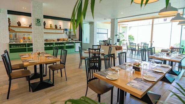 A restaurant with multiple dining tables, chairs, and a kitchen area with shelves. - Hotel San Blas (Lima)