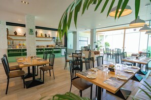 A restaurant with multiple dining tables, chairs, and a kitchen area with shelves. - Hotel San Blas (Lima)