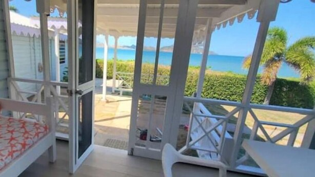 Een balkon met uitzicht op zee, een witte stoel en een bank met een rood-wit patroon.
