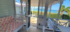 Un balcón con vista al mar, una silla blanca y un sofá con estampado rojo y blanco.