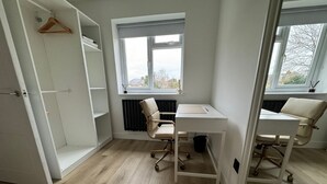 Quarto com escrivaninha, duas cadeiras, radiador e janela com vista.