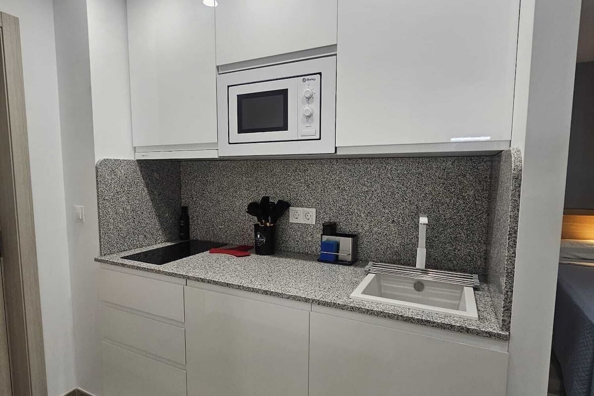 A modern kitchen with white cabinets, a built-in microwave, granite countertops, and a stainless steel sink.