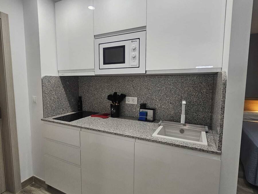 A modern kitchen with white cabinets, a built-in microwave, granite countertops, and a stainless steel sink.
