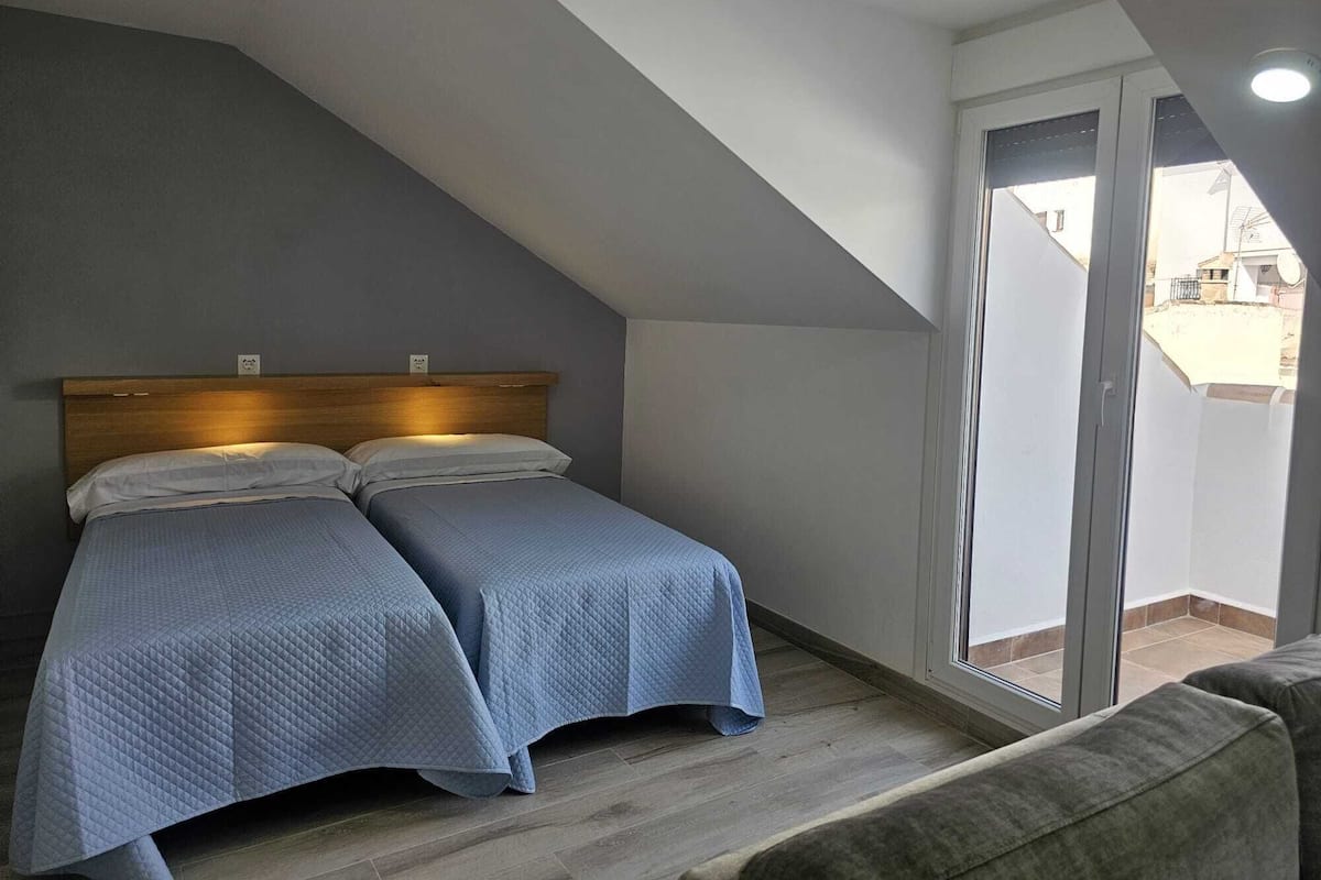 A bedroom with two beds, a sloped ceiling, and a sliding glass door to the outside.