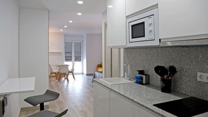 A modern kitchen with white cabinets, a microwave, a sink, and a countertop with kitchen utensils. - Apartamentos Antequera (Antequera)