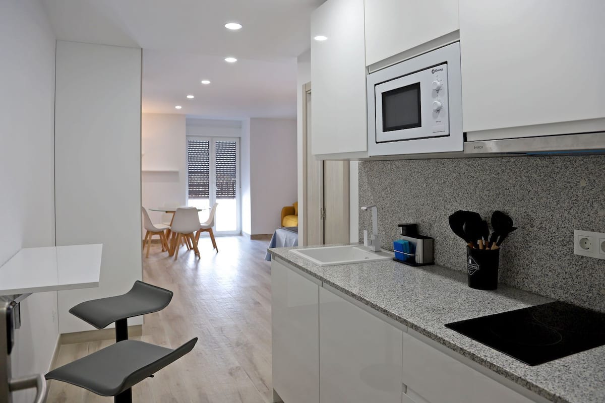 A modern kitchen with white cabinets, a microwave, a sink, and a countertop with kitchen utensils.