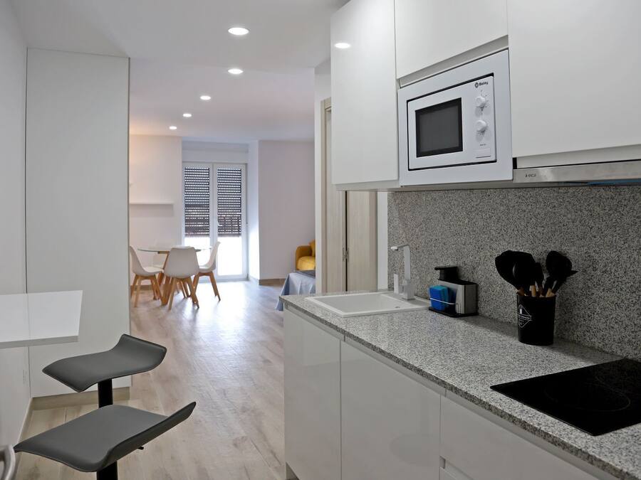 A modern kitchen with white cabinets, a microwave, a sink, and a countertop with kitchen utensils.