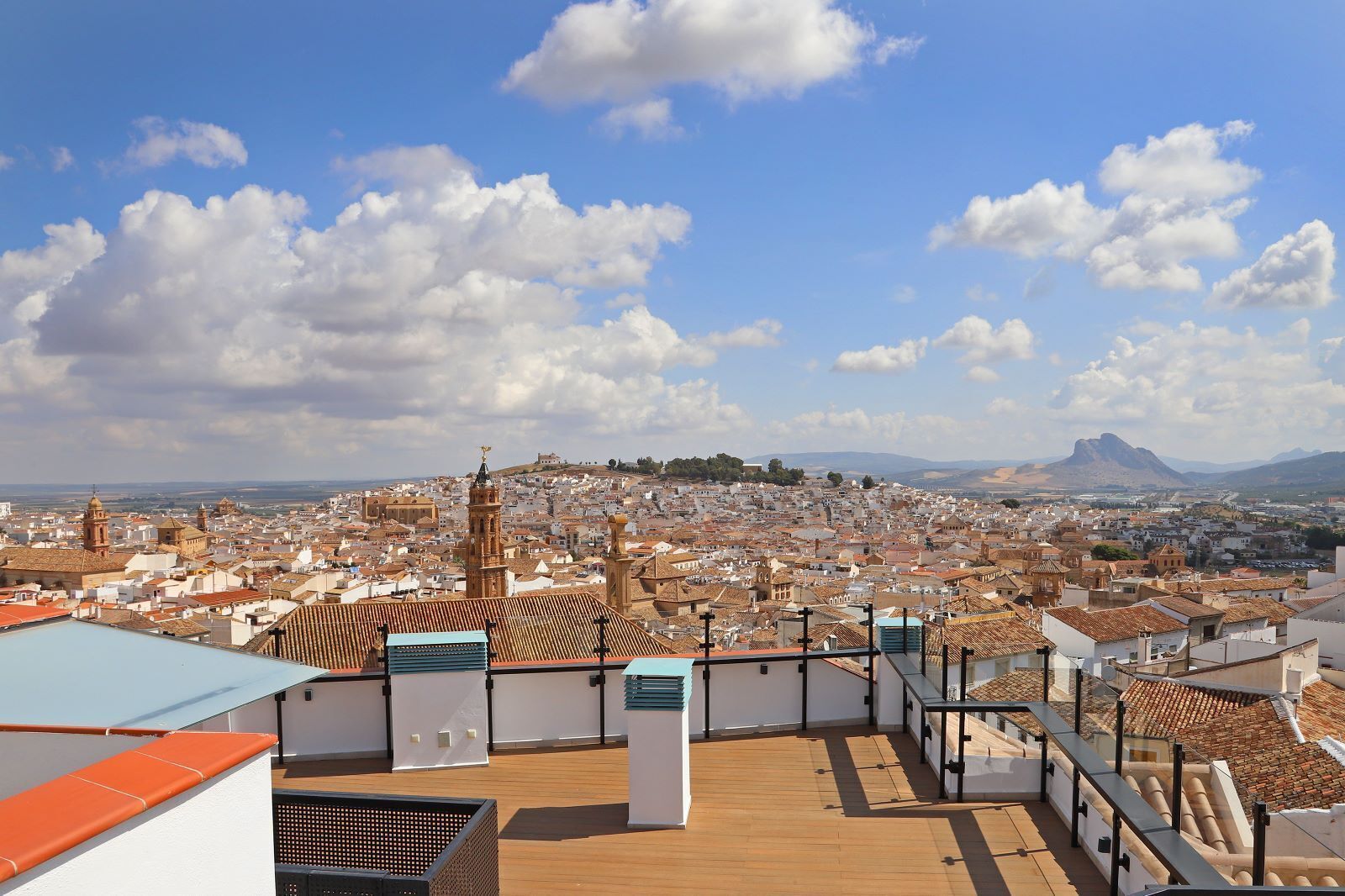 Una terraza en la azotea con vistas a un paisaje urbano, que incluye edificios históricos y una montaña a lo lejos.