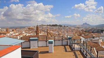 Una terraza en la azotea con vistas a un paisaje urbano, que incluye edificios históricos y una montaña a lo lejos.