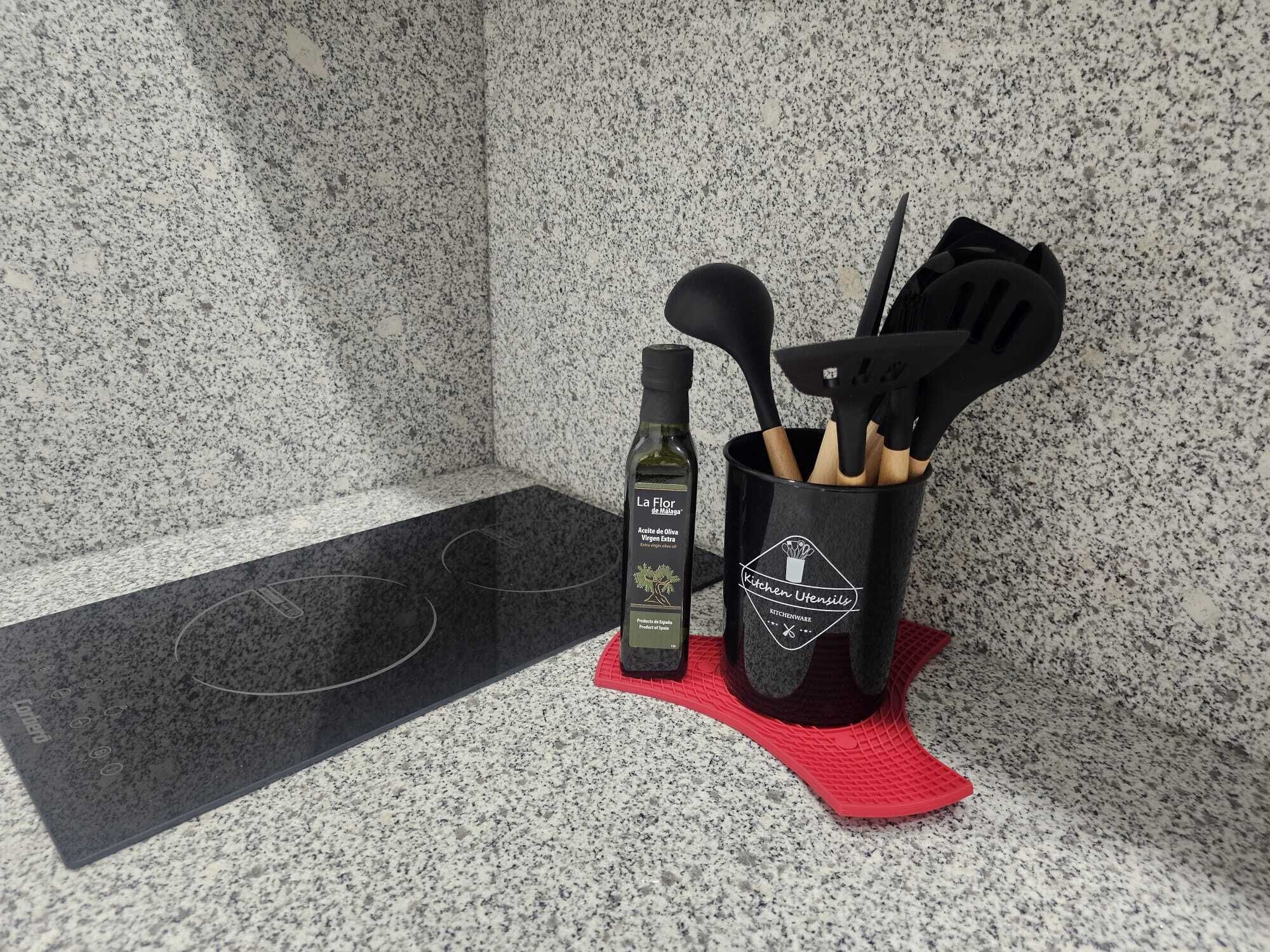 A kitchen area with a granite countertop, a bottle of olive oil, and a utensil holder with wooden utensils.