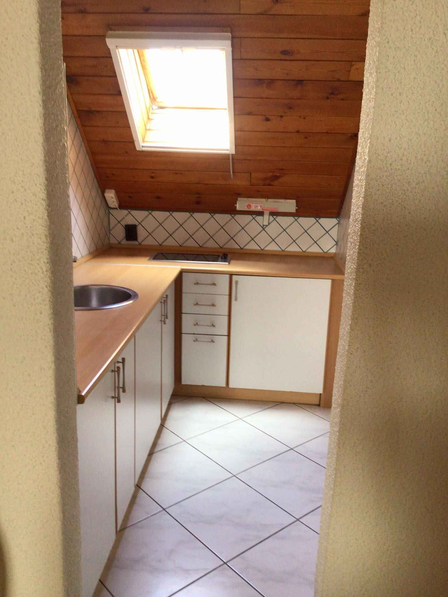 Una cocina compacta con techo de madera, una ventana pequeña, armarios blancos y piso de baldosas.