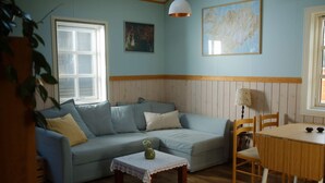 Een gezellige woonkamer met een lichtblauwe bank, een klein tafeltje met een vaas, houten stoelen en een eettafel.