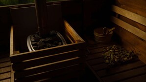Een sauna met een houten bank, een metalen rooster en een houten kom.