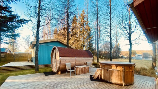 Een houten terras met een jacuzzi, een houten vatstructuur en een klein zitgedeelte met stoelen.