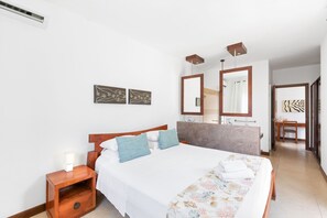 Hotellihuone, jossa on suuri sänky, yöpöytä lampun kanssa, peili ja taideteos seinällä.
