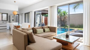 Ein modernes Wohnzimmer mit einer Eckcouch, einem Glastisch und Blick auf einen Swimmingpool.
