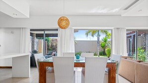 Ein modernes Wohnzimmer mit Essbereich, weißen Korbmöbeln und Blick auf einen Garten.