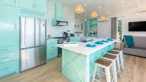 A modern kitchen with teal cabinetry, a stainless steel refrigerator, a microwave, and a central island with stools.