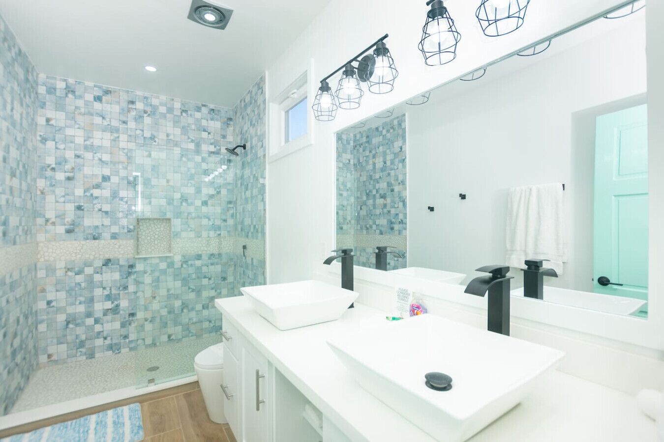 A modern bathroom with two sinks, a shower, and a large mirror.
