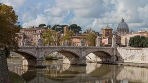 Un pont de pierre enjambant une rivière, avec une vue sur la ville en arrière-plan, notamment une structure en forme de dôme.
