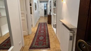 Un couloir avec un tapis à motifs, des murs blancs et un radiateur.