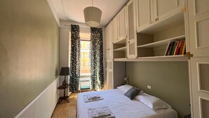 Une chambre à coucher comprenant un lit, une table de chevet, une lampe, une fenêtre avec des rideaux et des étagères intégrées remplies de livres.