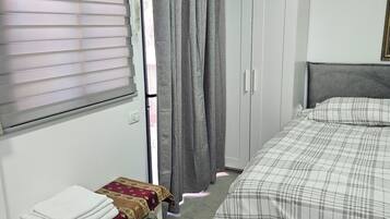 Een slaapkamer met een bed, nachtkastje, kledingkast en raam met zonwering.